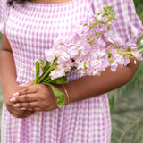 Person wearing a purple checkered dress holding pink flowers with a blurred green background