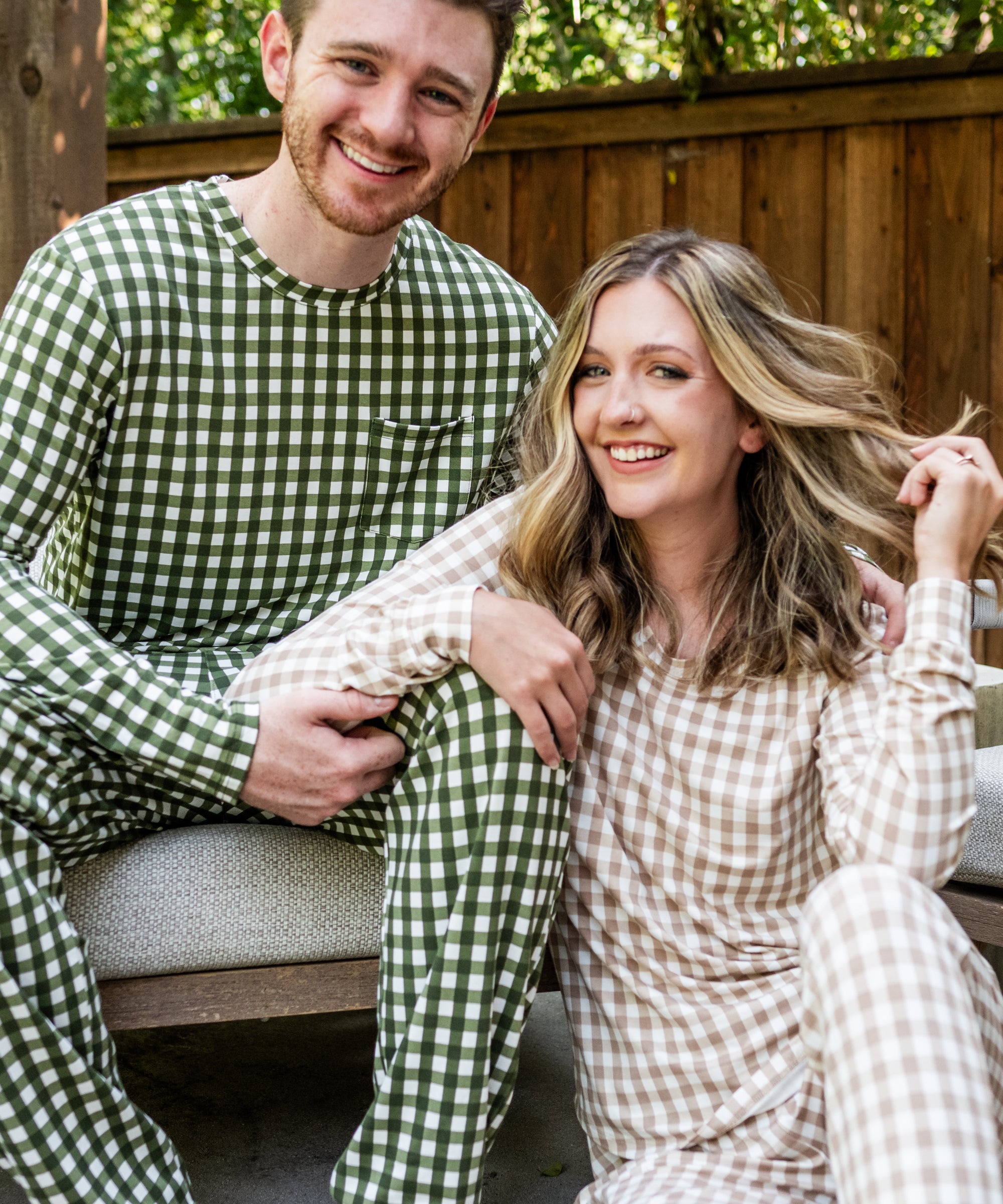 Male model sitting on a bench wearing the Jogger Set in Gingham Fir while woman sits on floor wearing the Jogger Set in Gingham Bisque