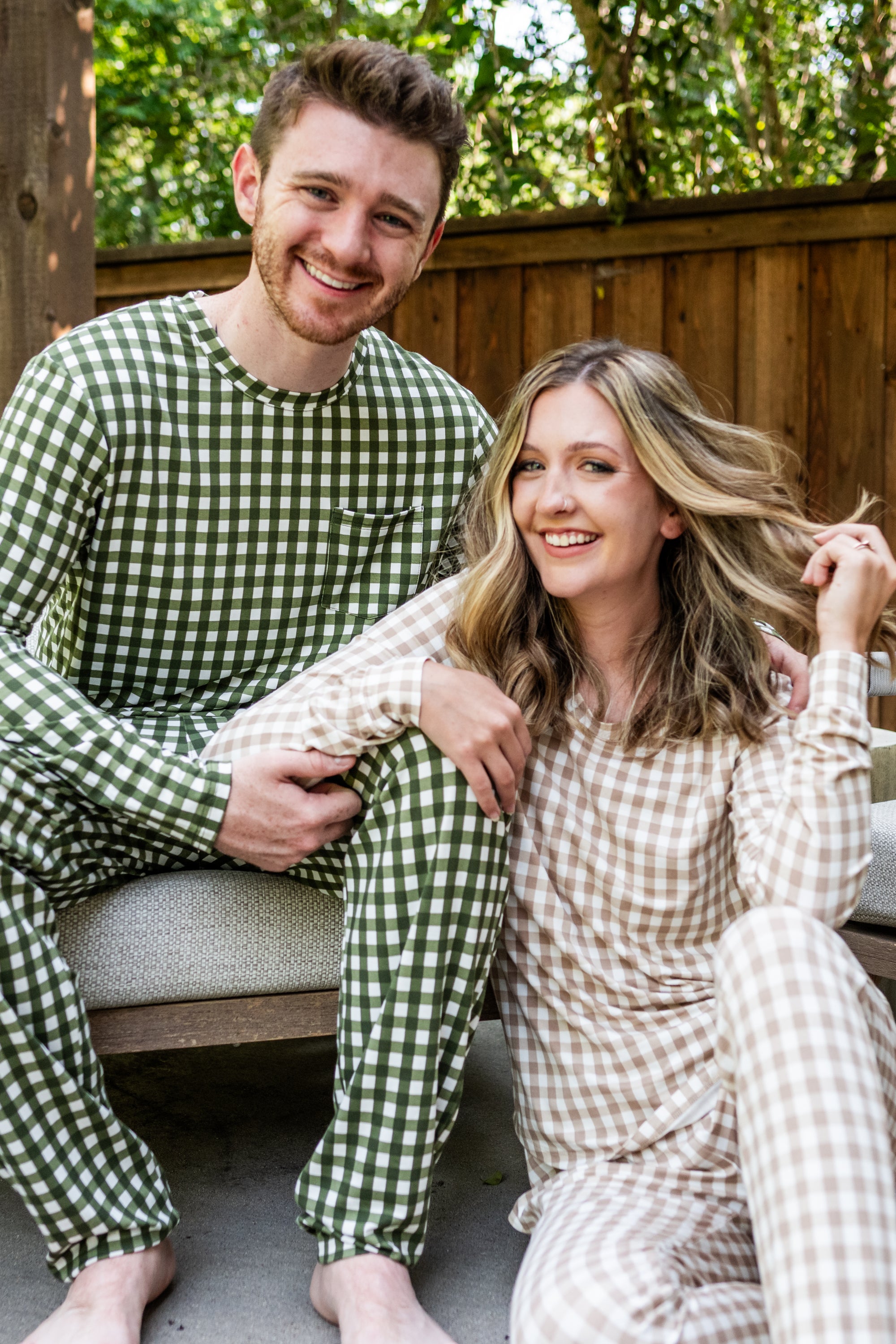 Male model sitting on a bench wearing the Jogger Set in Gingham Fir while woman sits on floor wearing the Jogger Set in Gingham Bisque