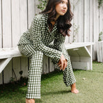 Woman in green checkered pajamas sitting on grass next to a wooden bench.