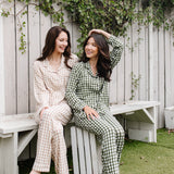 Models sitting on a bench while wearing the Kyte Women's Long Sleeve Pajama in Bisque and Fir Gingham