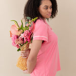 Woman modeling Women’s Short Sleeve Pajama Set in Guava with Cloud Trim holding a bouquet behind back