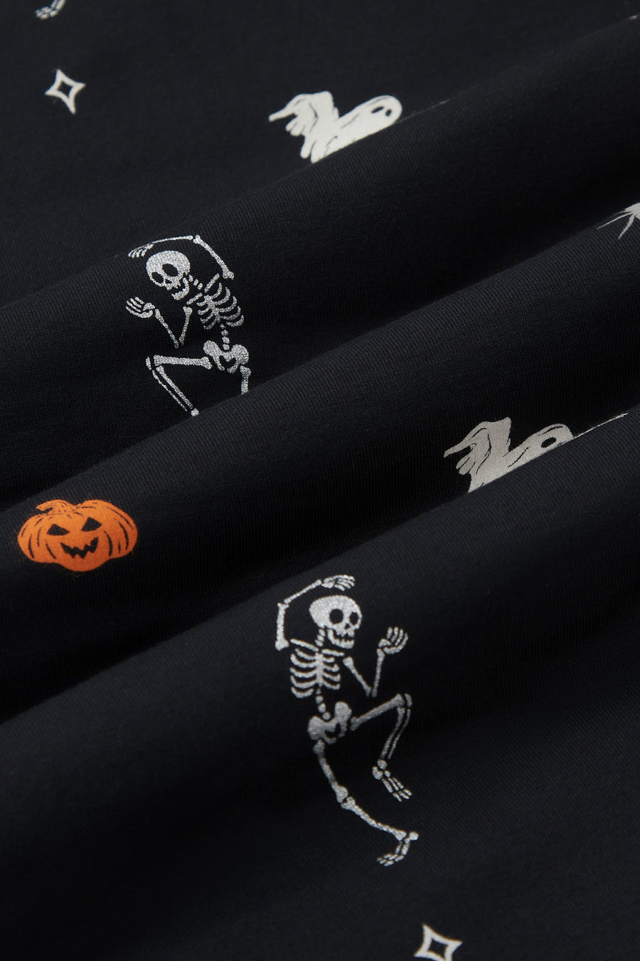 A repeating, all-over print featuring a flying white ghost, an orange jack o’ lantern, a dancing grey skeleton, a grey spider, and various white and grey twinkles, over a black background.