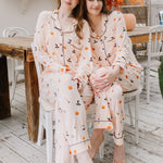 Two women in matching halloween pajamas sitting on a chair in a cozy room.