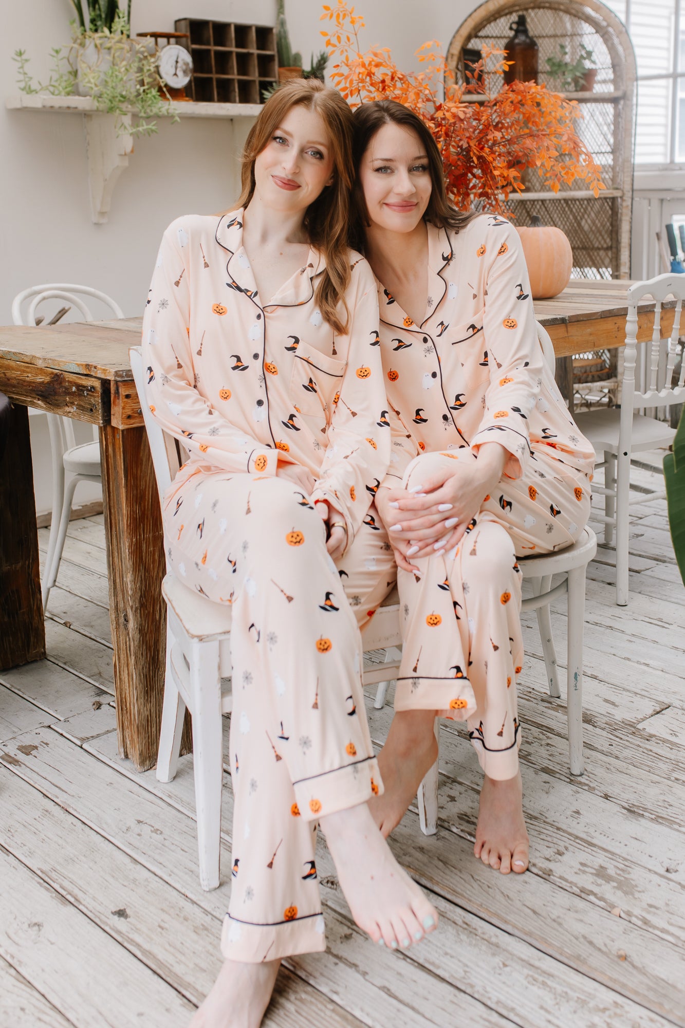 Two women in matching halloween pajamas sitting on a chair in a cozy room.