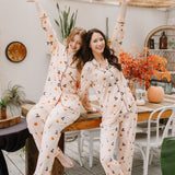 Two women in matching halloween pajamas sitting on a wooden table in a cozy room.