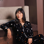 Modal sitting against a sofa wearing a Black Long-Sleeved Women's Pajama Set in Halloween Friends print ---PJ 4