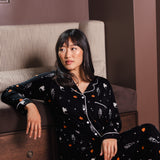Modal sitting against a sofa wearing a Black Long-Sleeved Women's Pajama Set in Halloween Friends print ---PJ 4