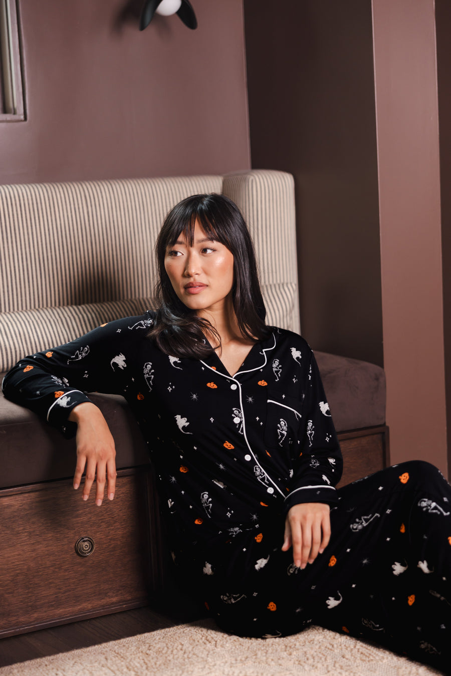 Modal sitting against a sofa wearing a Black Long-Sleeved Women's Pajama Set in Halloween Friends print