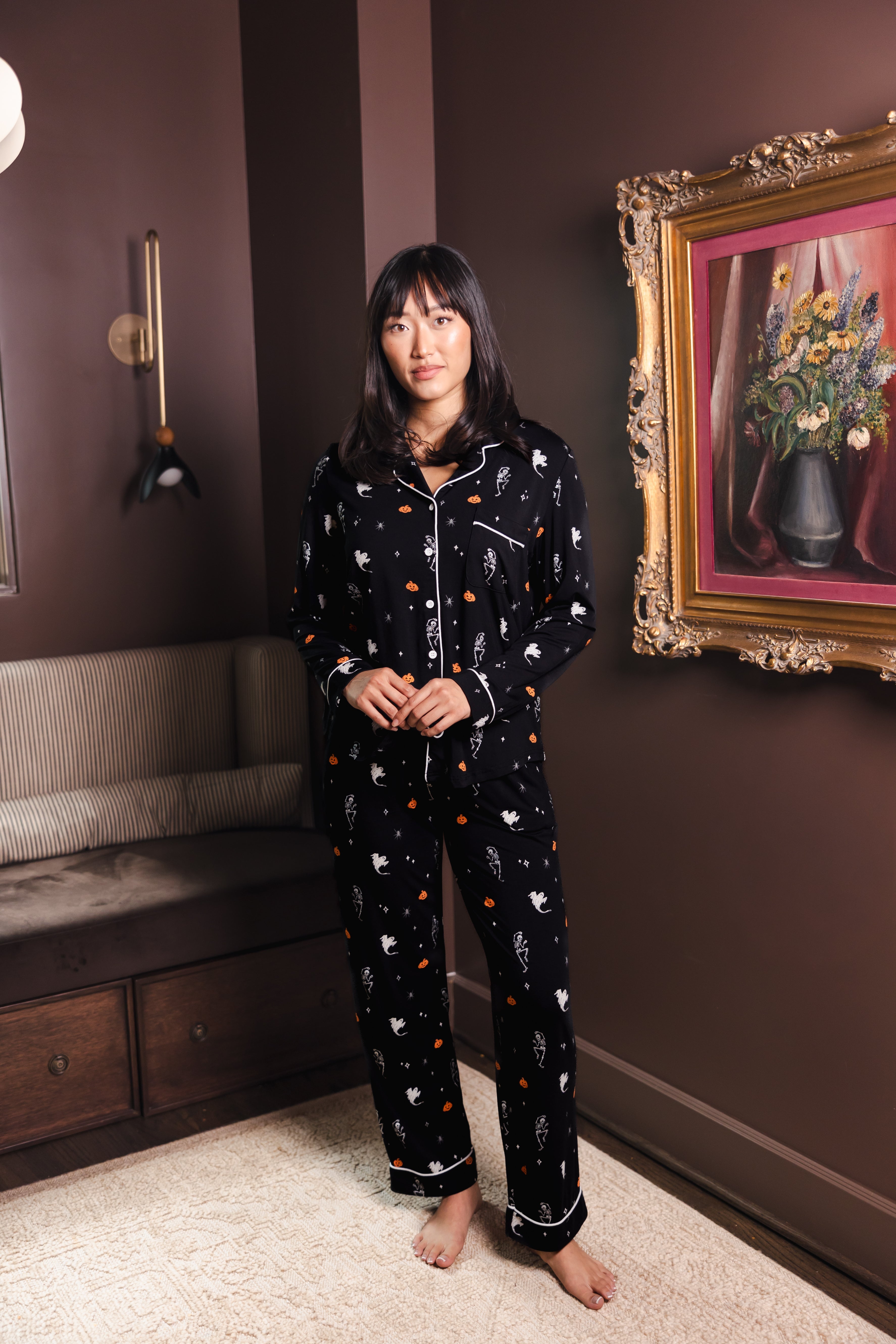 Modal wearing Black Long-Sleeved Women's Pajama Set in Halloween Friends print standing in a living room ::: Model is 5'9" wearing size S /// ---1605 3