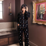 Modal wearing Black Long-Sleeved Women's Pajama Set in Halloween Friends print standing in a living room 