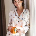 Modal standing against a wall holding a cup wearing a Beige Long-Sleeved Women's Pajama Set in Halloween Teddy print ---PJ 4