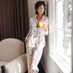 Modal standing against a wall holding a cup wearing a Beige Long-Sleeved Women's Pajama Set in Halloween Teddy print