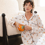 Modal sitting against a white sofa wearing Beige Long-Sleeved Women's Pajama Set in Halloween Teddy print while holding a mug ---1605 1