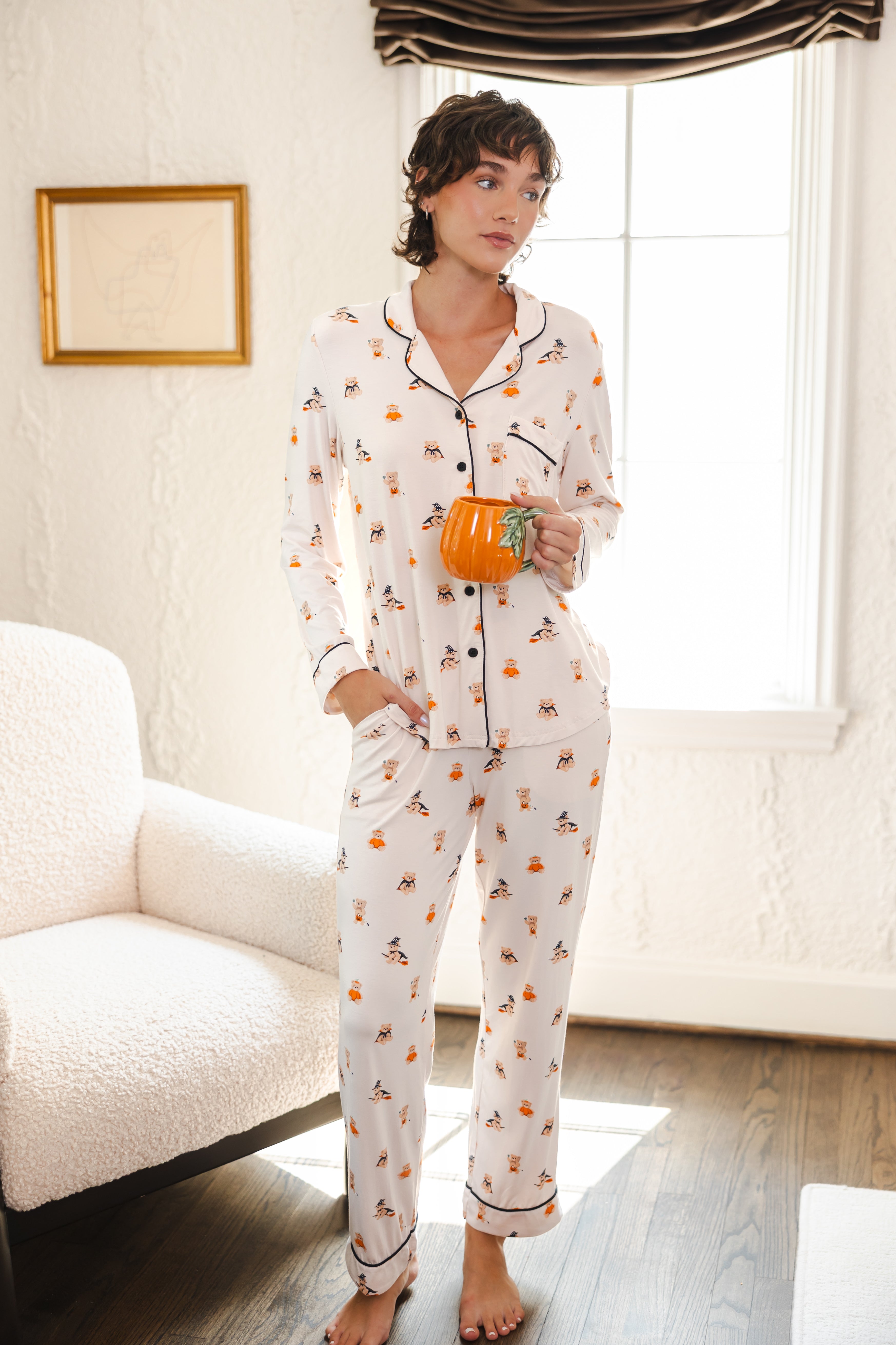 Modal wearing Beige Long-Sleeved Women's Pajama Set in Halloween Teddy print holding a mug standing in a living room ::: Model is 5'10" wearing size XS ///