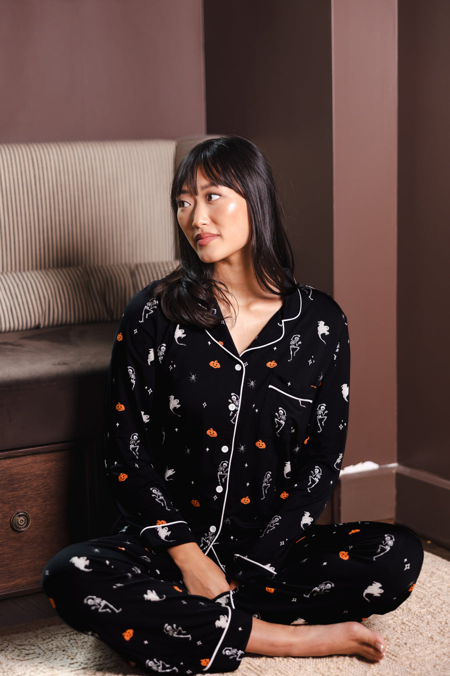 Modal sitting in front of sofa in Black Long-Sleeved Women's Pajama Set in Halloween Friends print