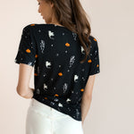 Back side of Modal wearing Women's Oversized V-Neck Tee in Halloween Friends print over white pants on a beige background