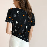 Back side of Modal wearing Women's Oversized V-Neck Tee in Halloween Friends print over white pants on a beige background