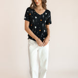 Modal posing in Women's Oversized V-Neck Tee in Halloween Friends print over white pants on a beige background