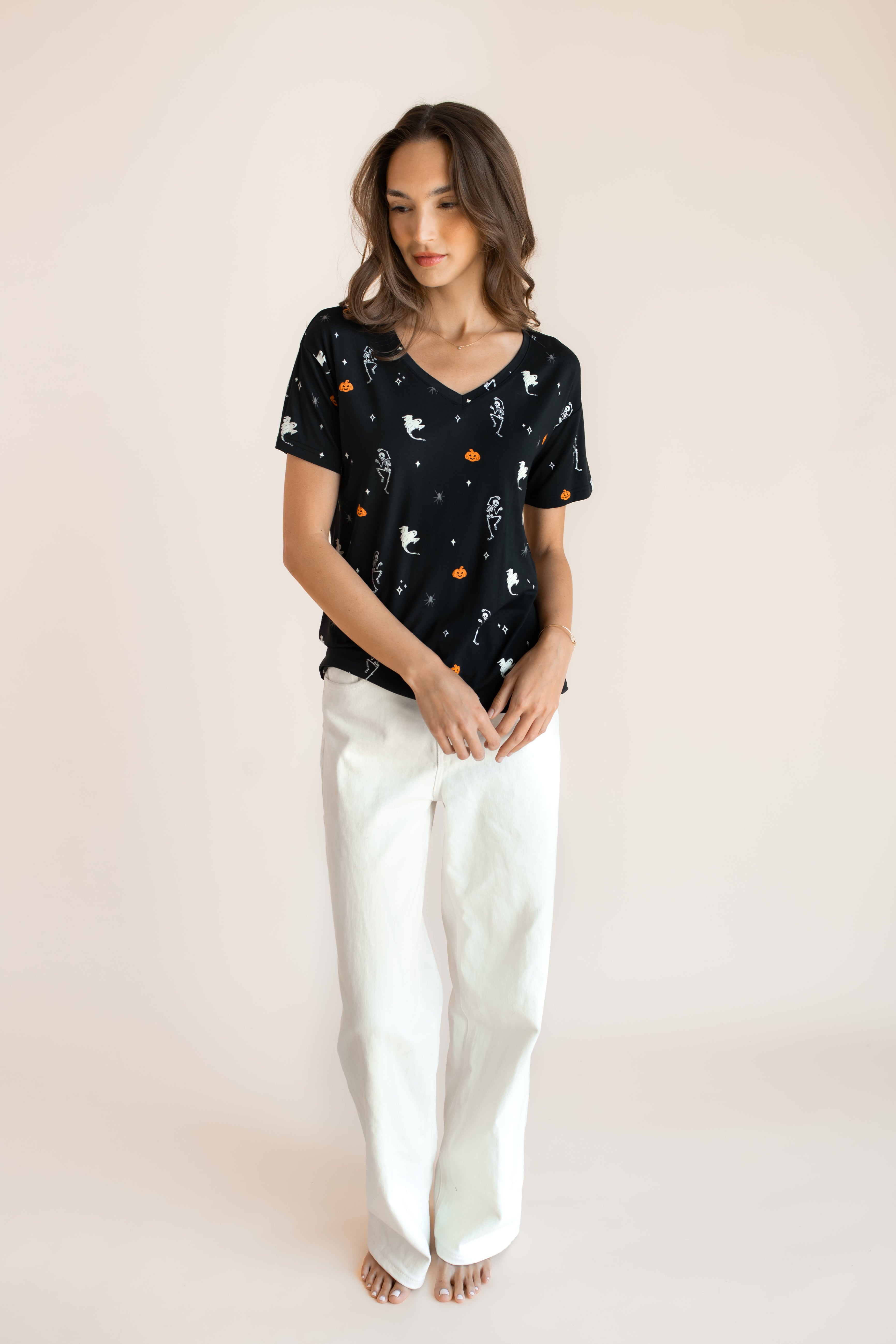 Modal posing in Women's Oversized V-Neck Tee in Halloween Friends print over white pants on a beige background