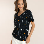 Close up of Modal in Women's Oversized V-Neck Tee in Halloween Friends print over white pants on a beige background