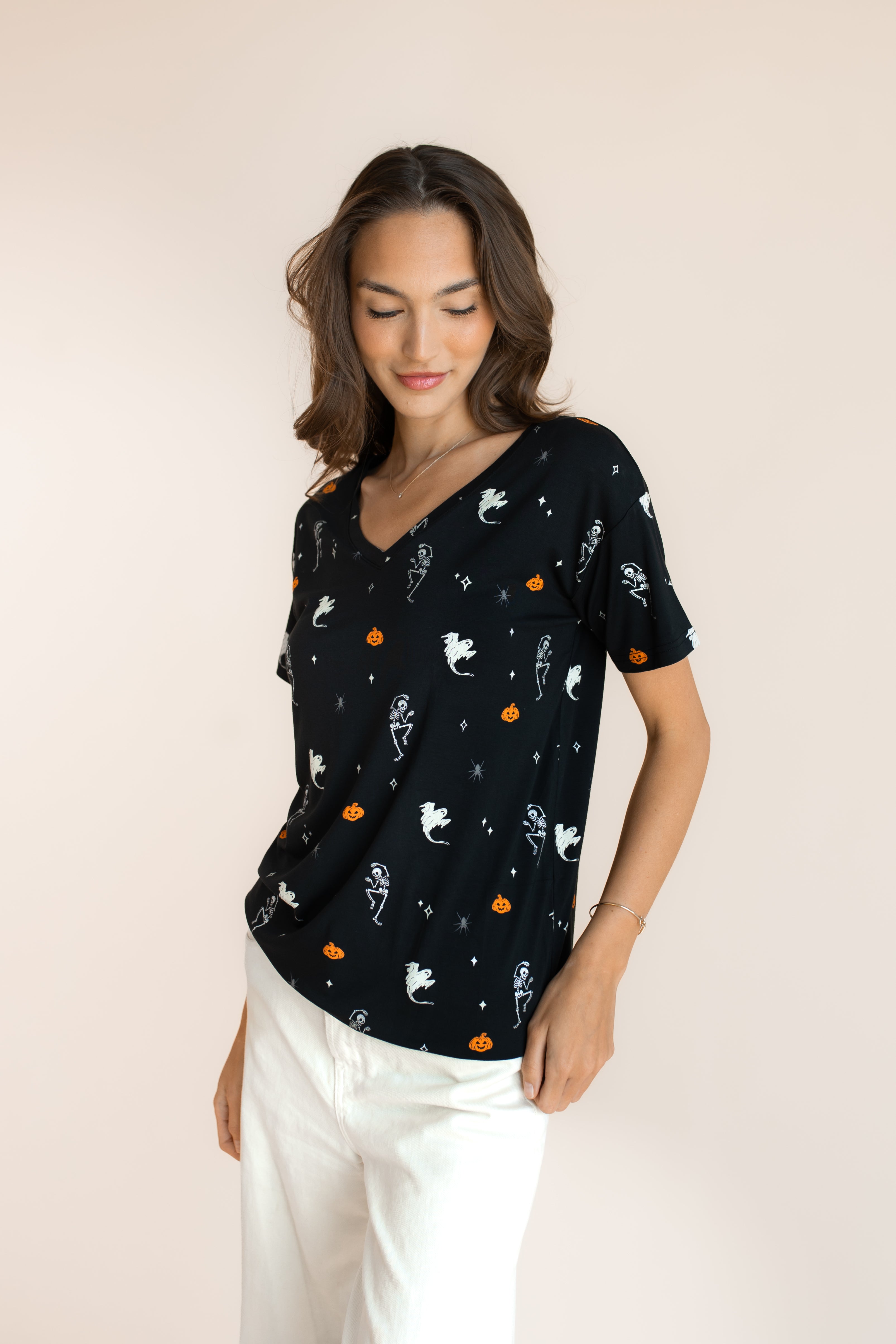 Close up of Modal in Women's Oversized V-Neck Tee in Halloween Friends print over white pants on a beige background