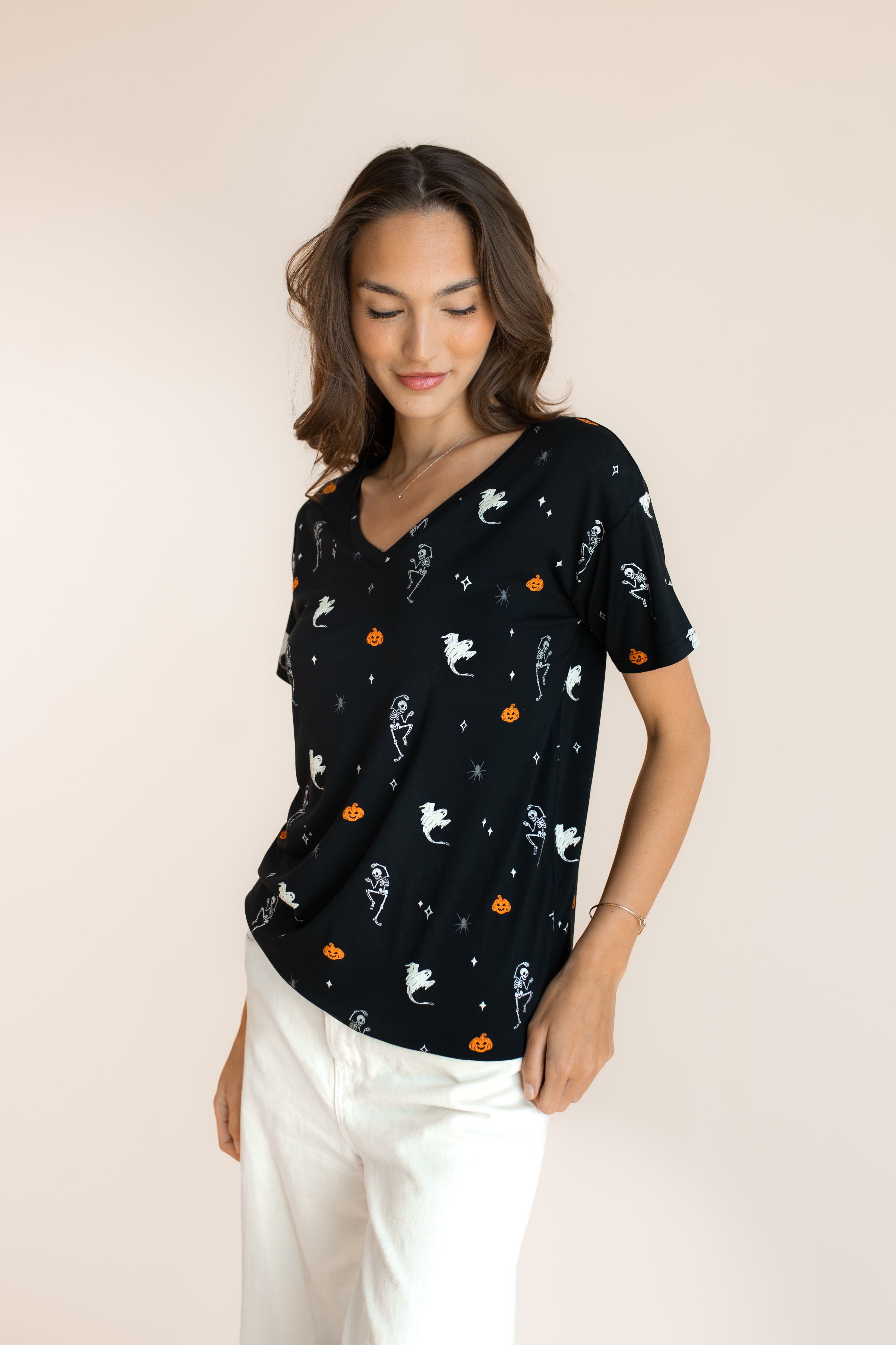 Close up of Modal in Women's Oversized V-Neck Tee in Halloween Friends print over white pants on a beige background