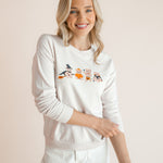 Modal posing in off white Women's Sweatshirt with Halloween Teddy print in the center over white pants standing in front of a beige background