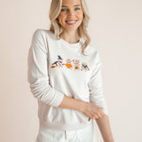 Modal posing in off white Women's Sweatshirt with Halloween Teddy print in the center over white pants standing in front of a beige background