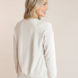 Back side of Modal wearing off white Women's Sweatshirt with Halloween Teddy print over white pants on a beige background