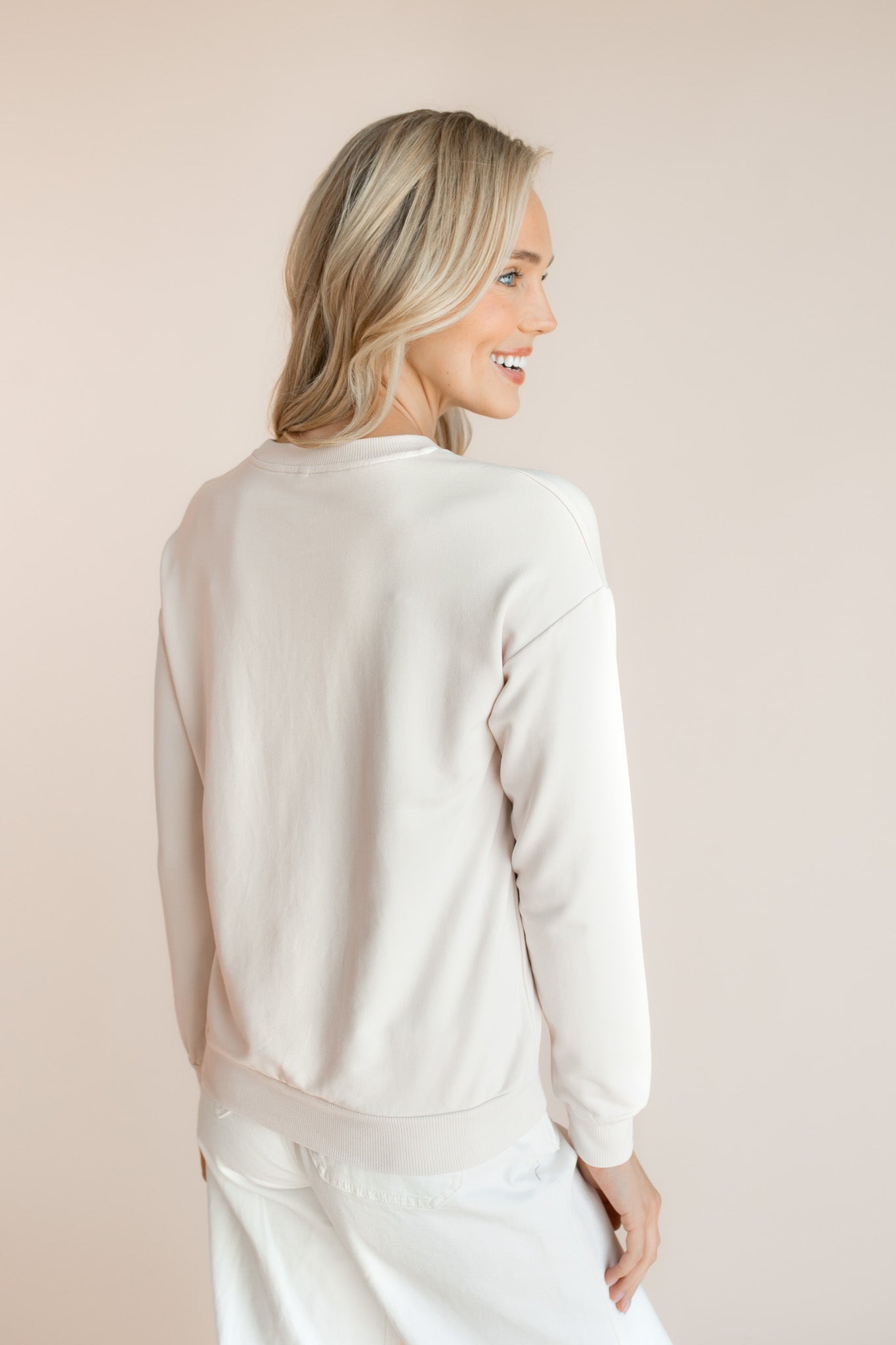 Back side of Modal wearing off white Women's Sweatshirt with Halloween Teddy print over white pants on a beige background