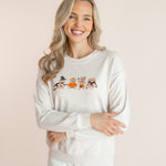 Modal wearing off white Women's Sweatshirt with Halloween Teddy print in the center over white pants smiling in front of a beige background