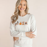 Modal wearing off white Women's Sweatshirt with Halloween Teddy print in the center over white pants smiling in front of a beige background