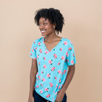 Woman wearing a blue floral Hibiscus v-neck tee and denim shorts against a beige background smiling 