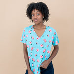 Woman wearing a blue floral Hibiscus v-neck tee and denim shorts against a beige background