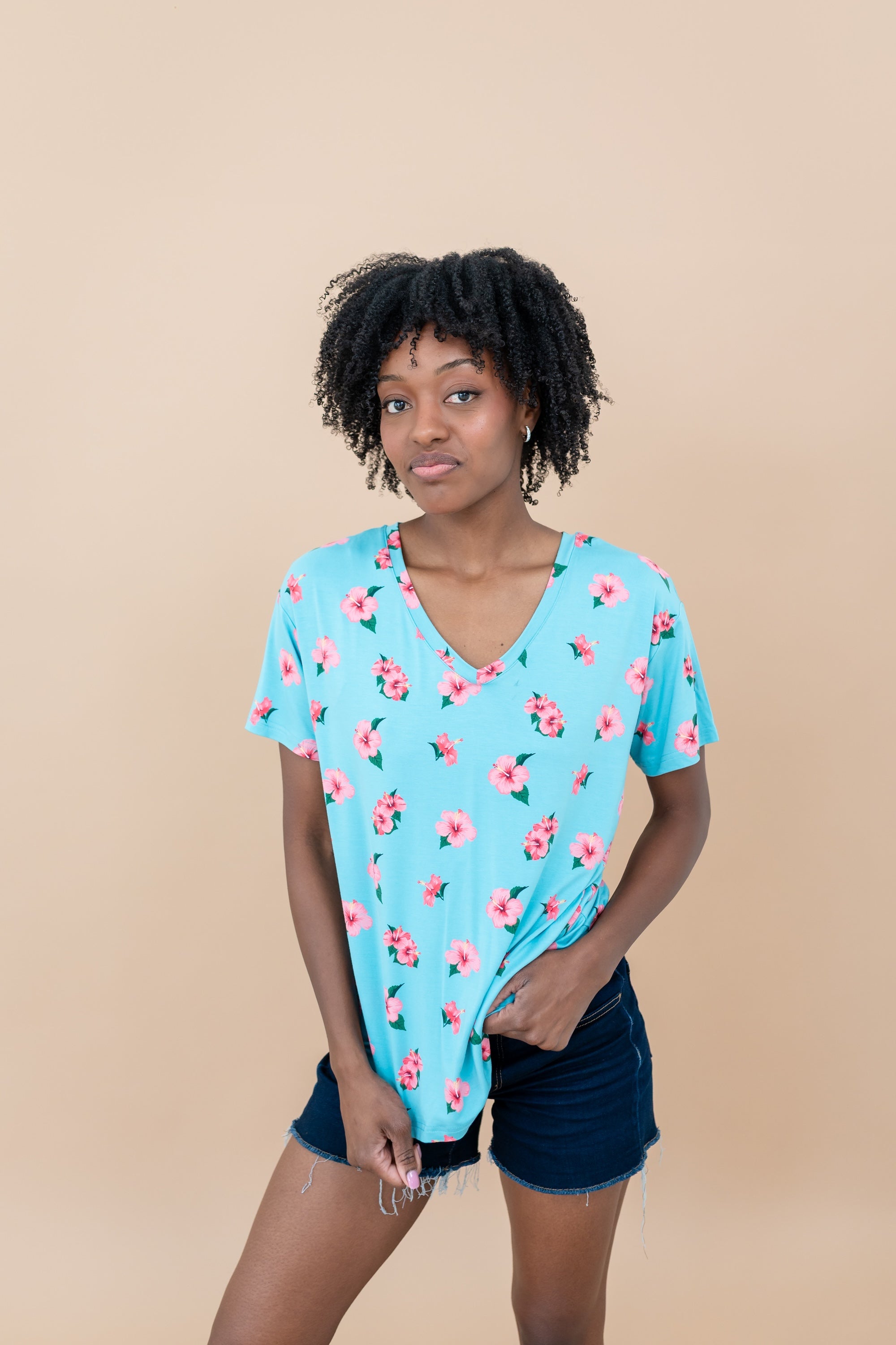 Woman wearing a blue floral Hibiscus v-neck tee and denim shorts against a beige background
