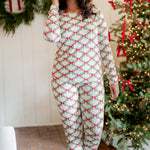 Female model standing in front of a white paneled wall and decorated Christmas tree wearing the Women's Jogger Pajama Set in Holiday Bow