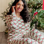 Smiling female model sitting on the floor wearing the Women's Jogger Pajama Set in Holiday Bow in front of a decorated Christmas Tree