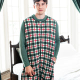 A man wearing a green, red, and white plaid hooded pajama sleep sack standing in a bedroom with a bed and large windows in the background.