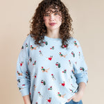 Woman wearing Women's Sweatshirt in Holiday Pups print over blue jeans on a beige background