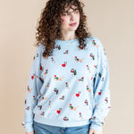 Woman posing in Women's Sweatshirt in Holiday Pups print over blue jeans on a beige background
