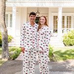 Couple wearing matching christmas pajamas with red truck and christmas tree pattern in front of a white house