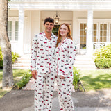 Couple wearing matching christmas pajamas with red truck and christmas tree pattern in front of a white house