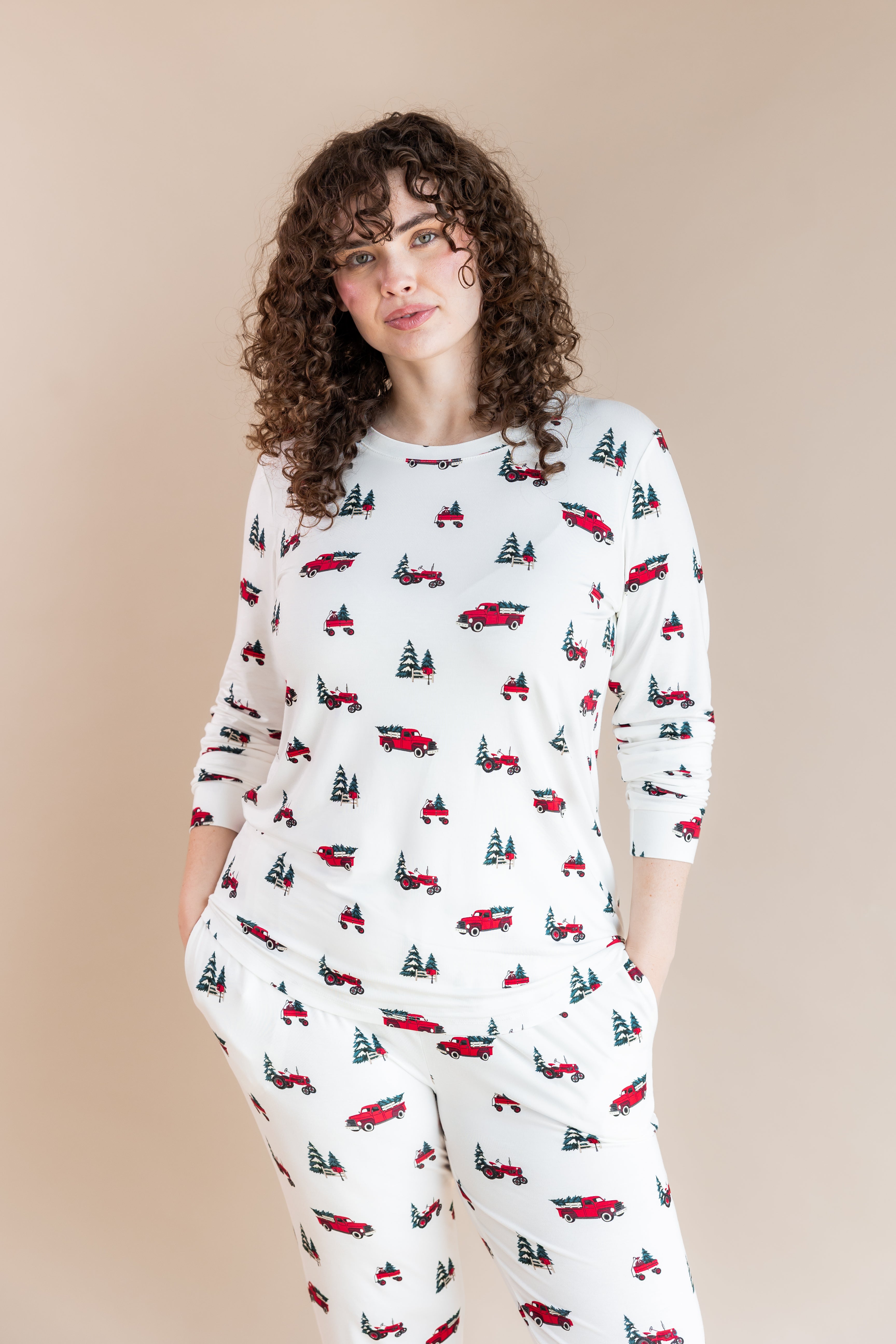 Woman soft smiling with her hands in her pajama pant pockets wearing a jogger pajama set in holiday tree farm