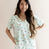 Model wearing Women's Relaxed Fit V-Neck having colorful Harry Potter patterns on a green and white striped fabric over beige pants on a beige background
