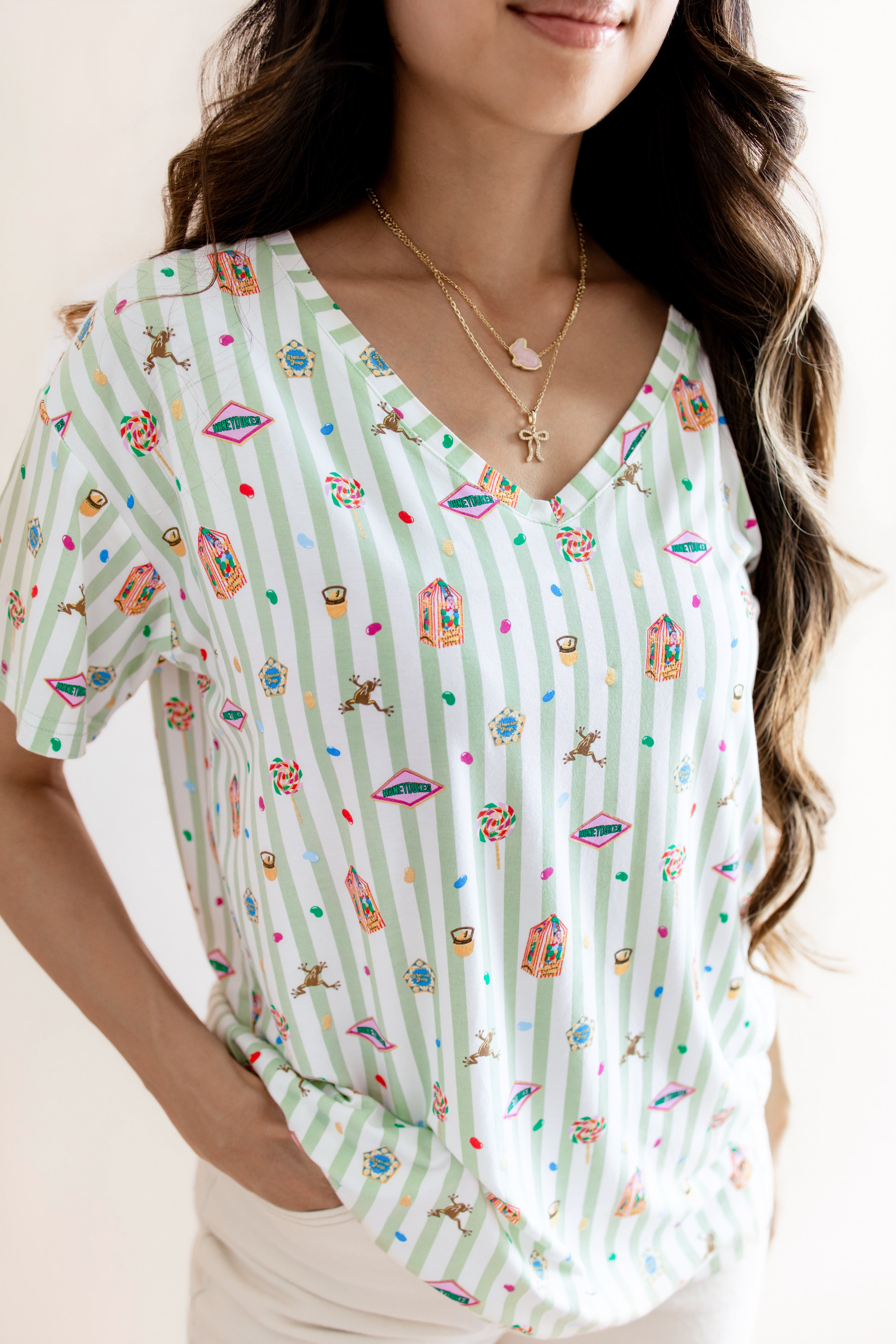 Model wearing Women's Relaxed Fit V-Neck having colorful Harry Potter patterns on a green and white striped fabric on a beige background

::: Model is 5'3" wearing size S ///


