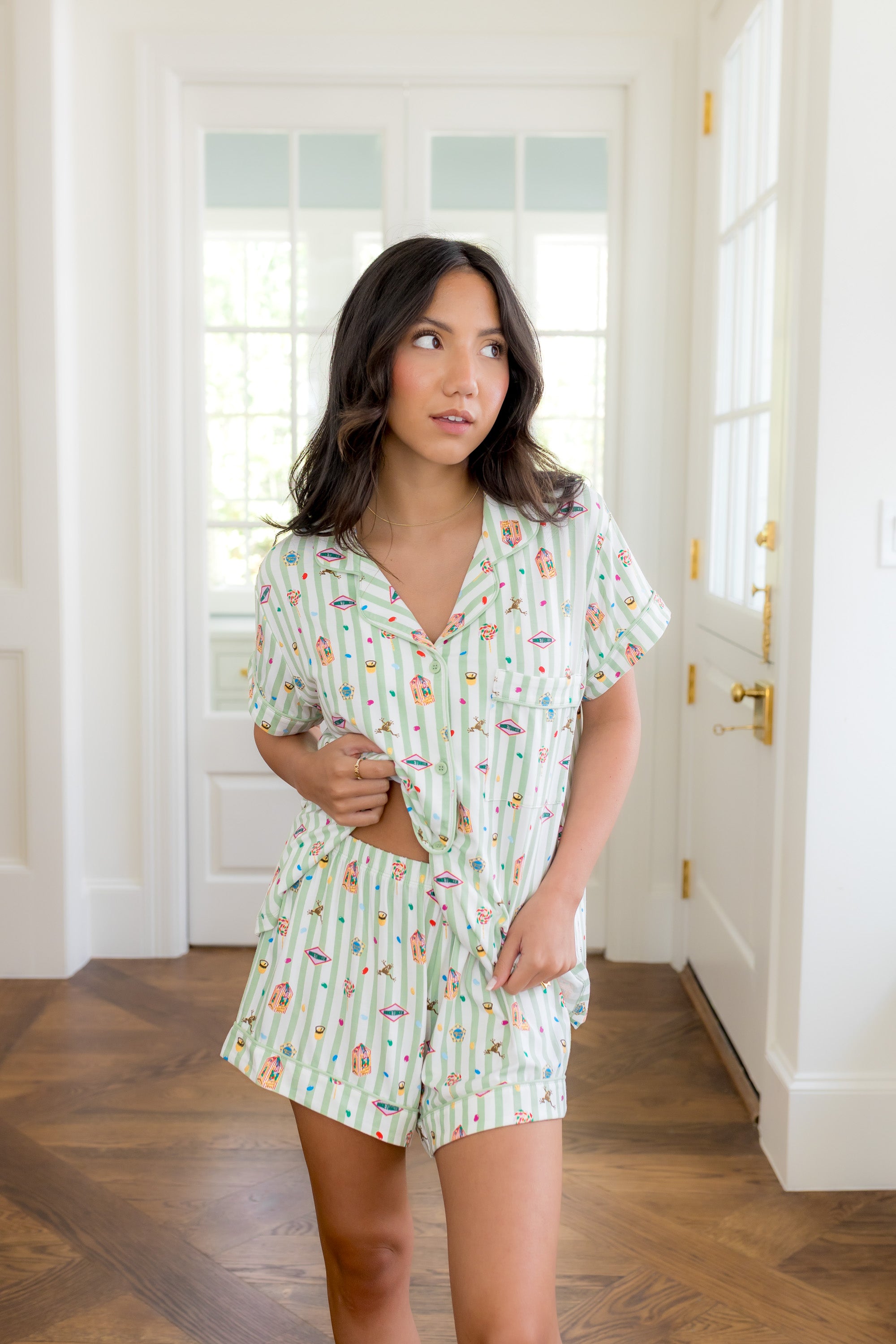 Woman in white room lifting bottom of top from the Women's Short Sleeve Pajama Set in Honeydukes and showcasing the waist band of the shorts   