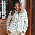 A woman wearing a long-sleeve pajama set with a colorful Harry Potter Honeydukes pattern on a white and light green striped background, standing in front of a wooden bookcase.
