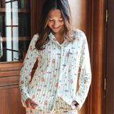 A woman wearing a long-sleeve pajama set with a colorful Harry Potter Honeydukes pattern on a white and light green striped background, standing in front of a wooden bookcase.