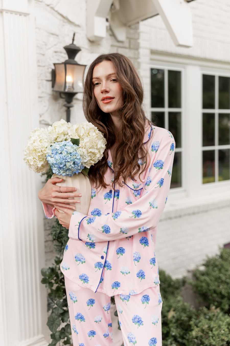 Woman outside holding a vase of hydrangeas in long sleeve pajamas in Hydrangea Sakura print.